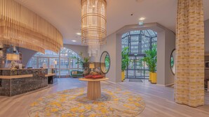 Una hall moderna con un tavolo rotondo al centro, una reception e un grande lampadario.