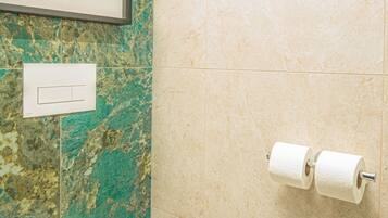 A bathroom with a toilet, a towel dispenser, and a framed picture on the wall.