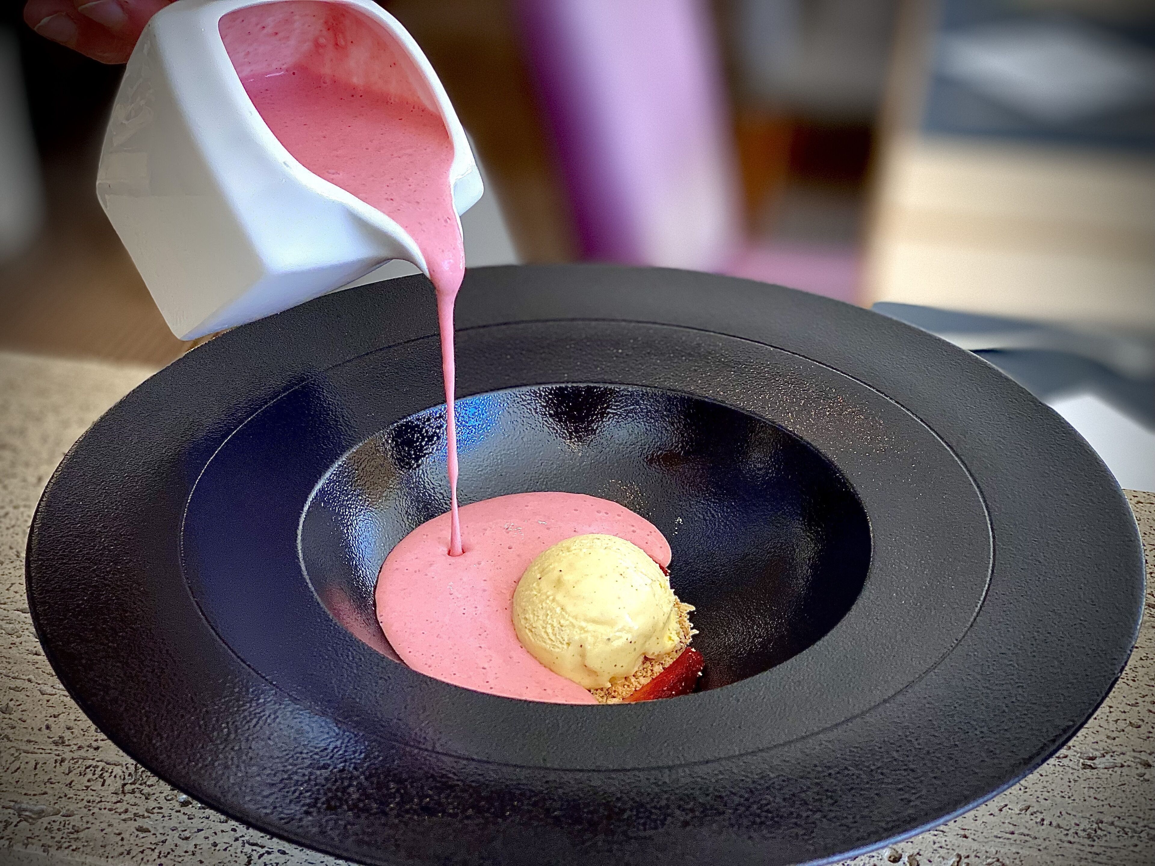 A dessert with pink sauce and a scoop of ice cream on a black plate.