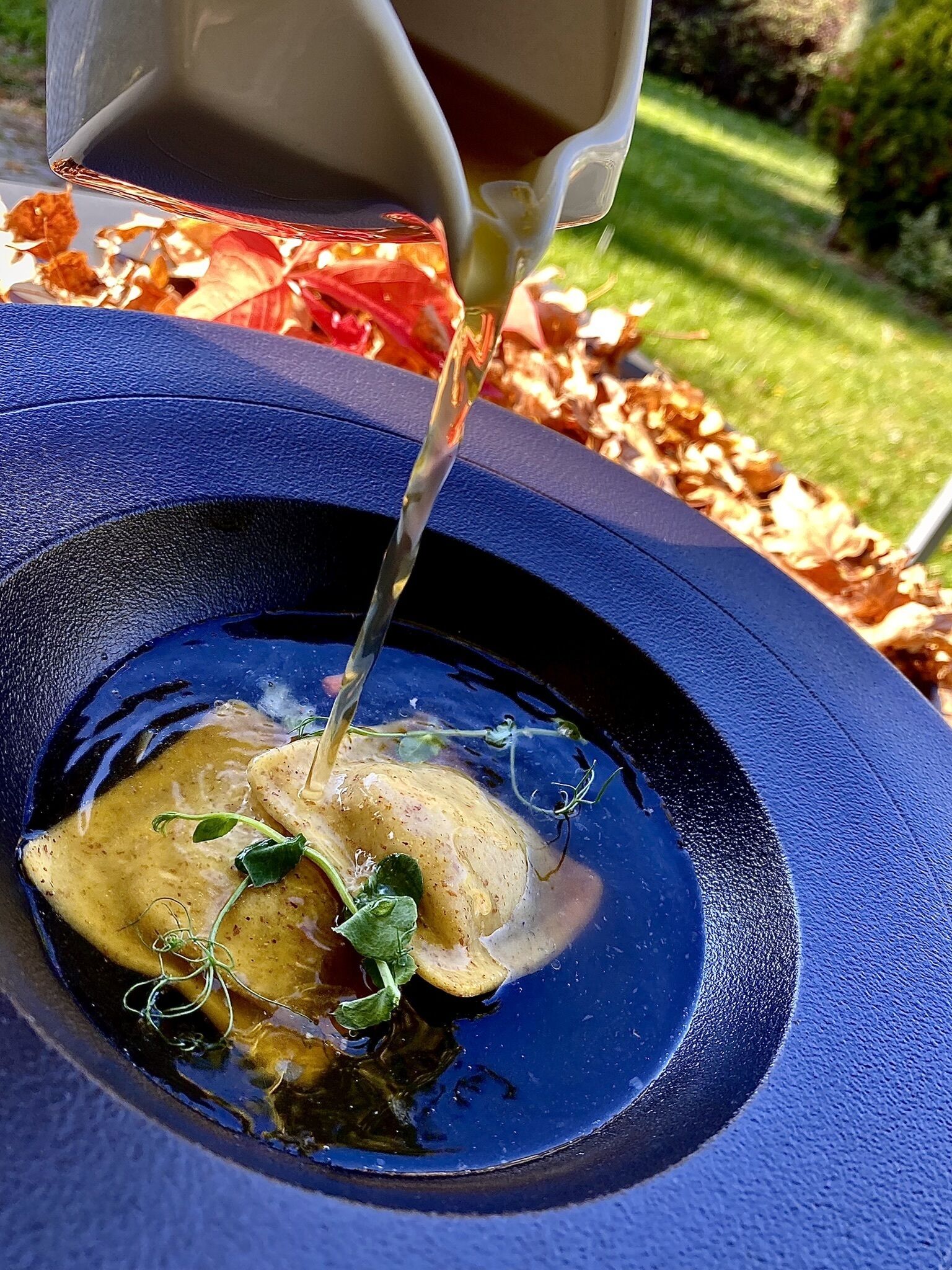 A bowl with a liquid being poured into it, containing a potato and some greens.