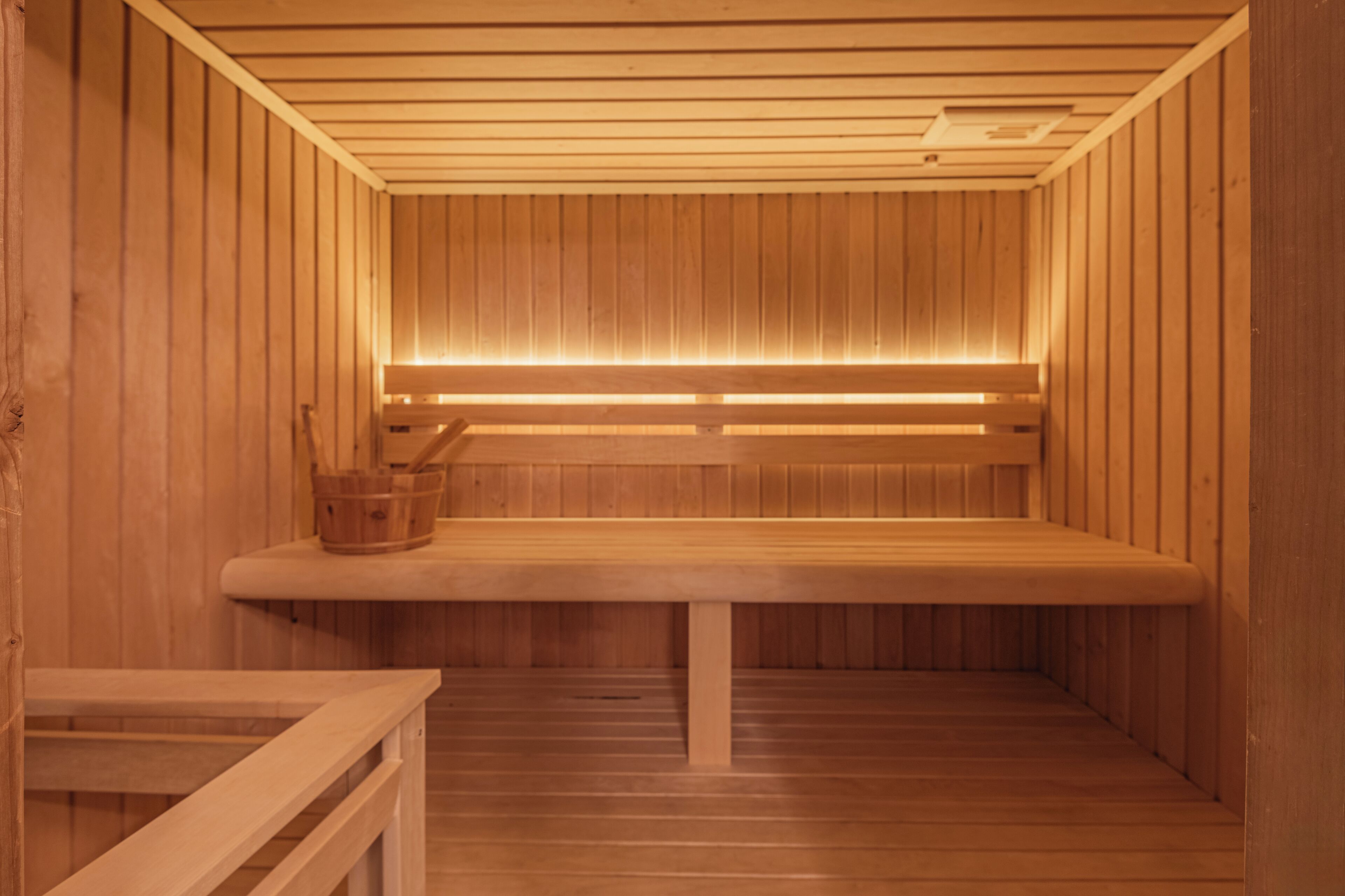 A wooden sauna with benches and a bench with a bucket.