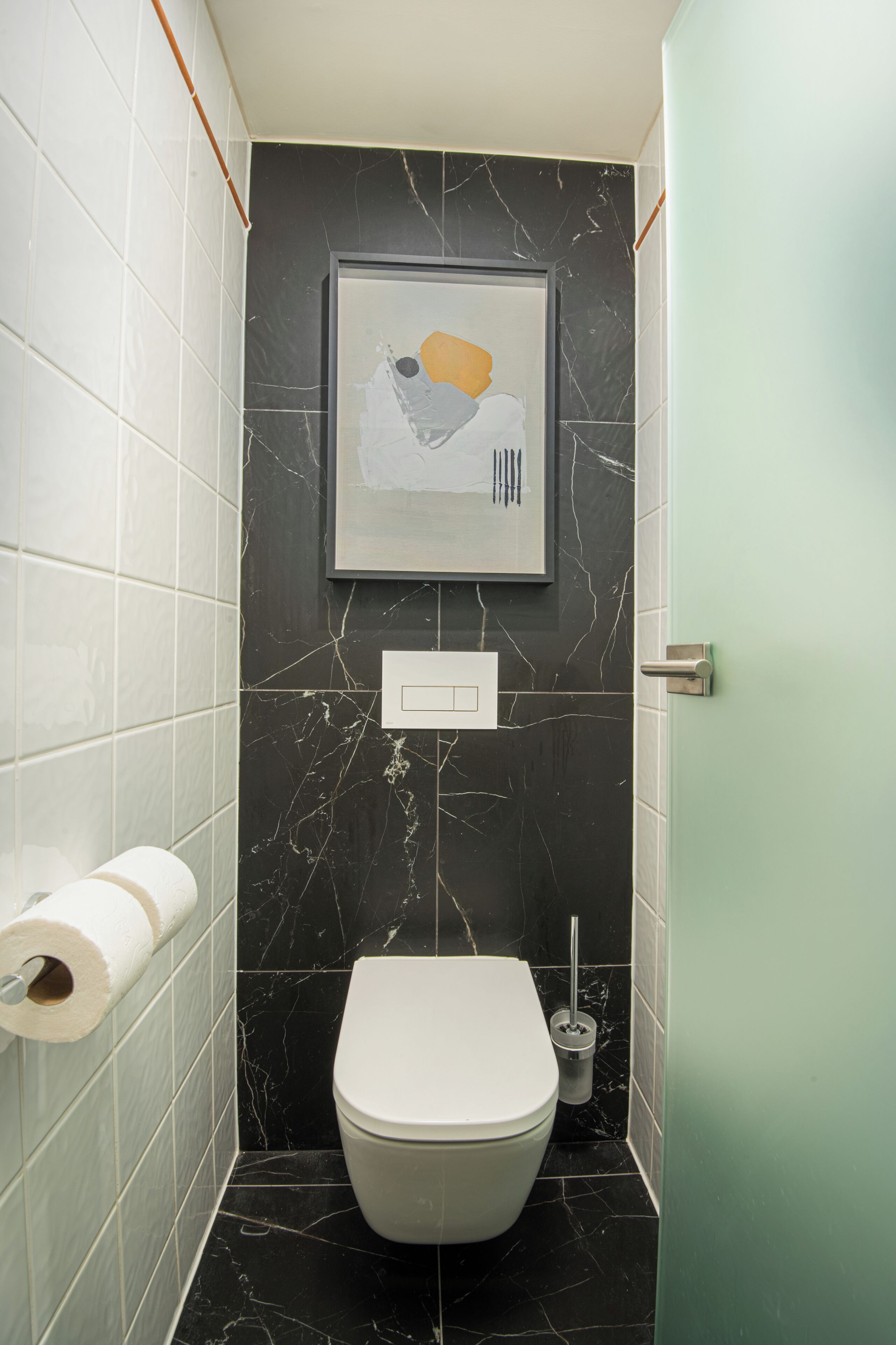 A bathroom with a toilet, a roll of toilet paper, a picture on the wall, and a light switch.