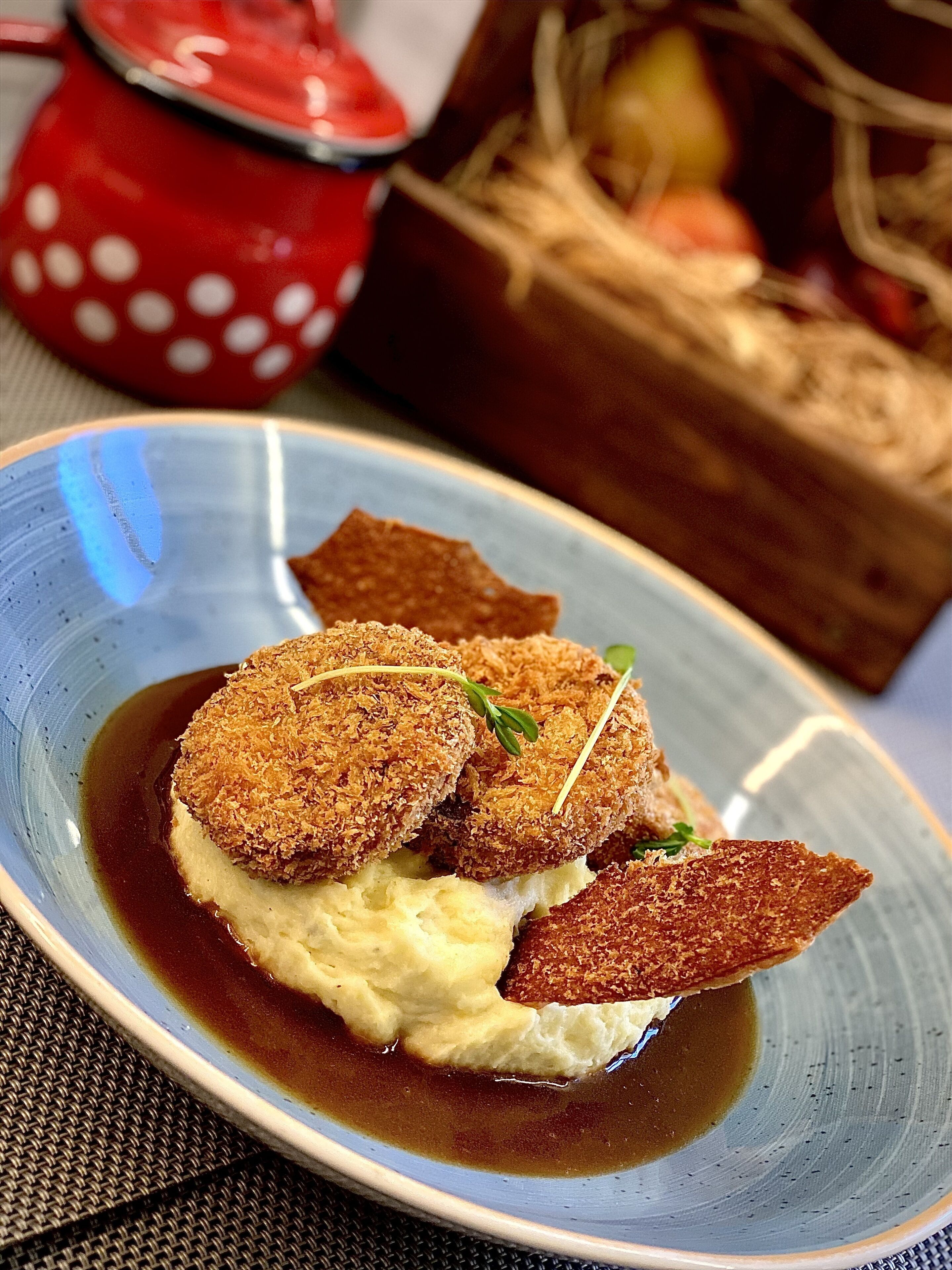 A plate of food with breaded items and mashed potatoes, accompanied by a small bowl of sauce.