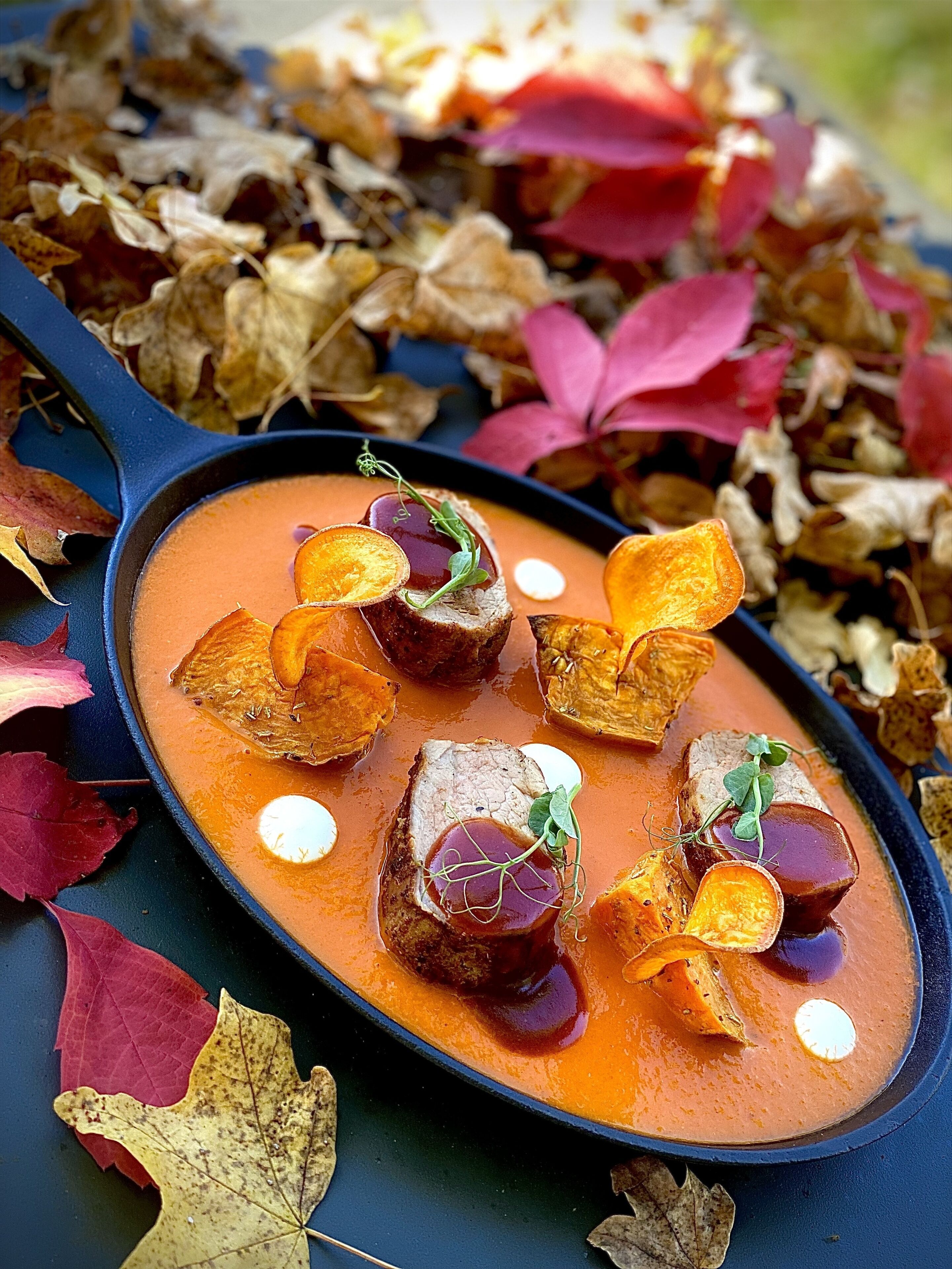 Eine Bratpfanne mit cremiger, oranger Soße, verziert mit Orangenscheiben und grünen Blättern, umgeben von Herbstlaub.