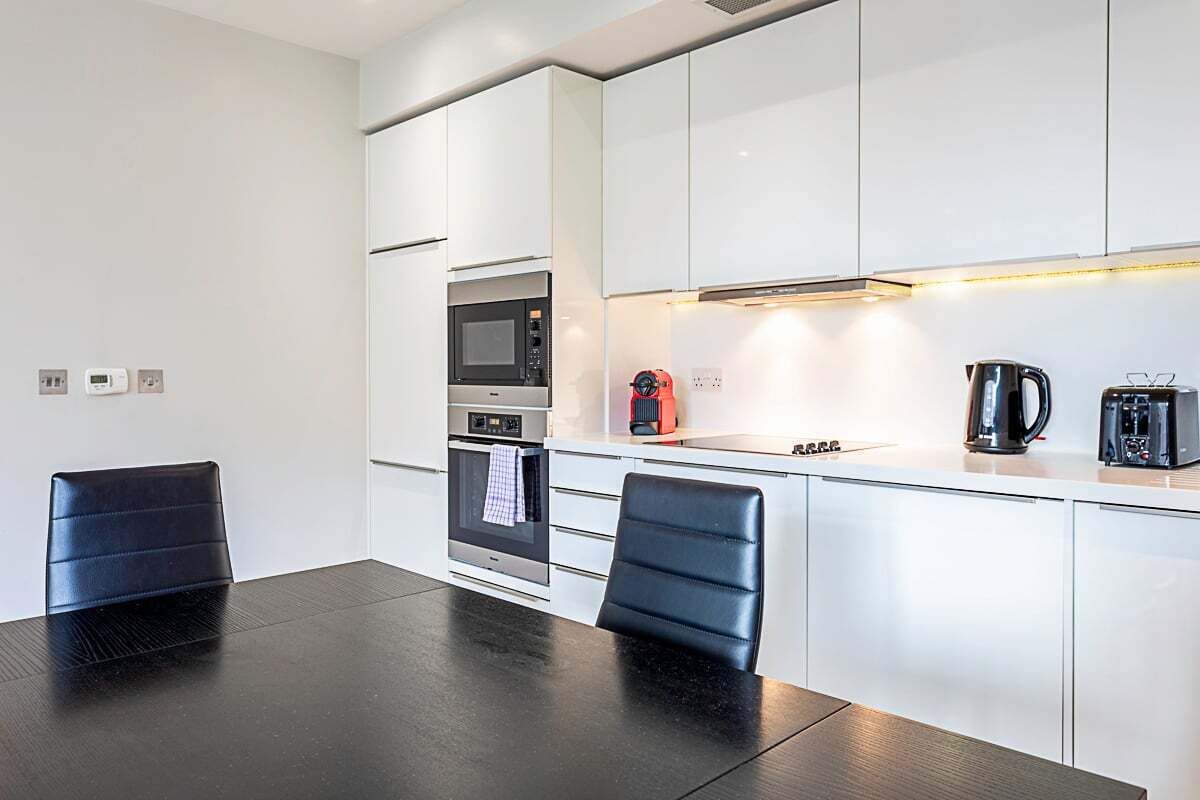 Een moderne keuken met witte kasten, een zwart aanrecht, een magnetron, een oven en een koffiezetapparaat.