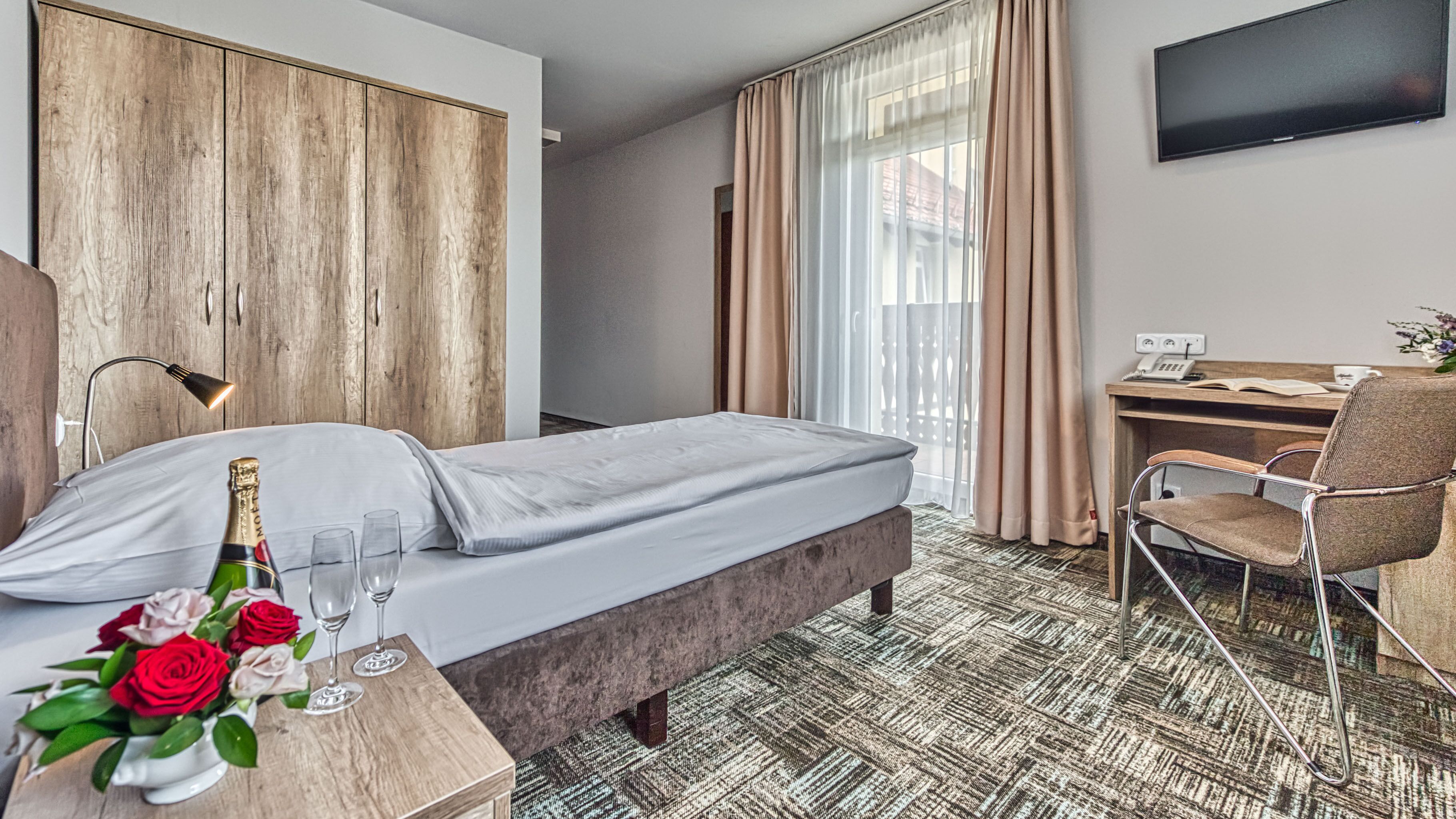 Une chambre d’hôtel équipée d’un lit, d’un bureau, d’une chaise, d’une télévision et d’une fenêtre avec des rideaux.