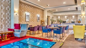 A hotel lobby with a reception desk, seating area with tables and chairs, and a patterned wall. - St. Lukas Medical & SPA (Swieradow-Zdroj)