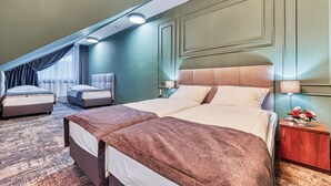 A hotel room with a large bed, a smaller bed, a sofa, a nightstand with a lamp, and a vase with flowers. - St. Lukas Medical & SPA (Swieradow-Zdroj)