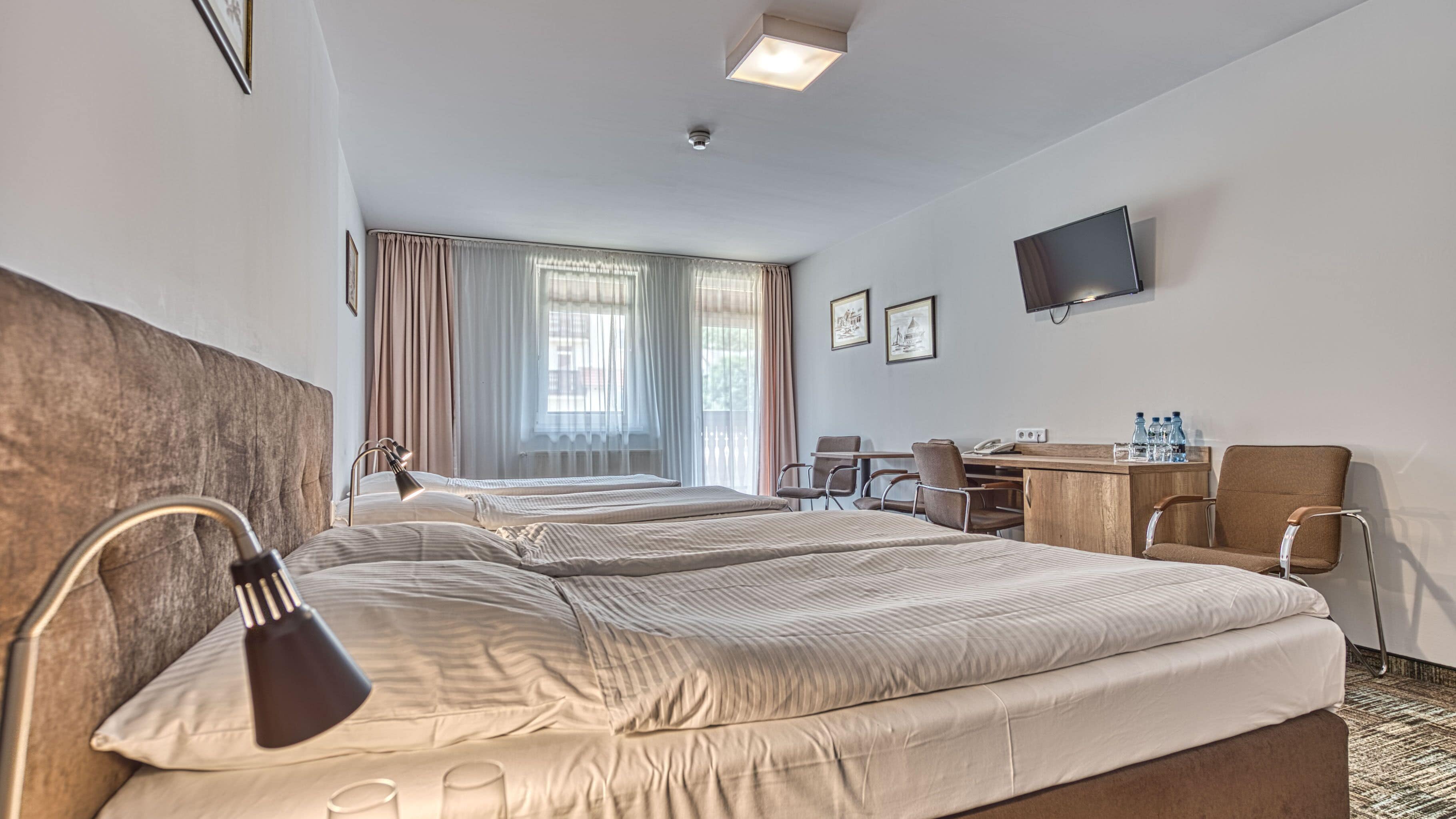A hotel room with two beds, a desk, a chair, a TV, and a window with curtains.