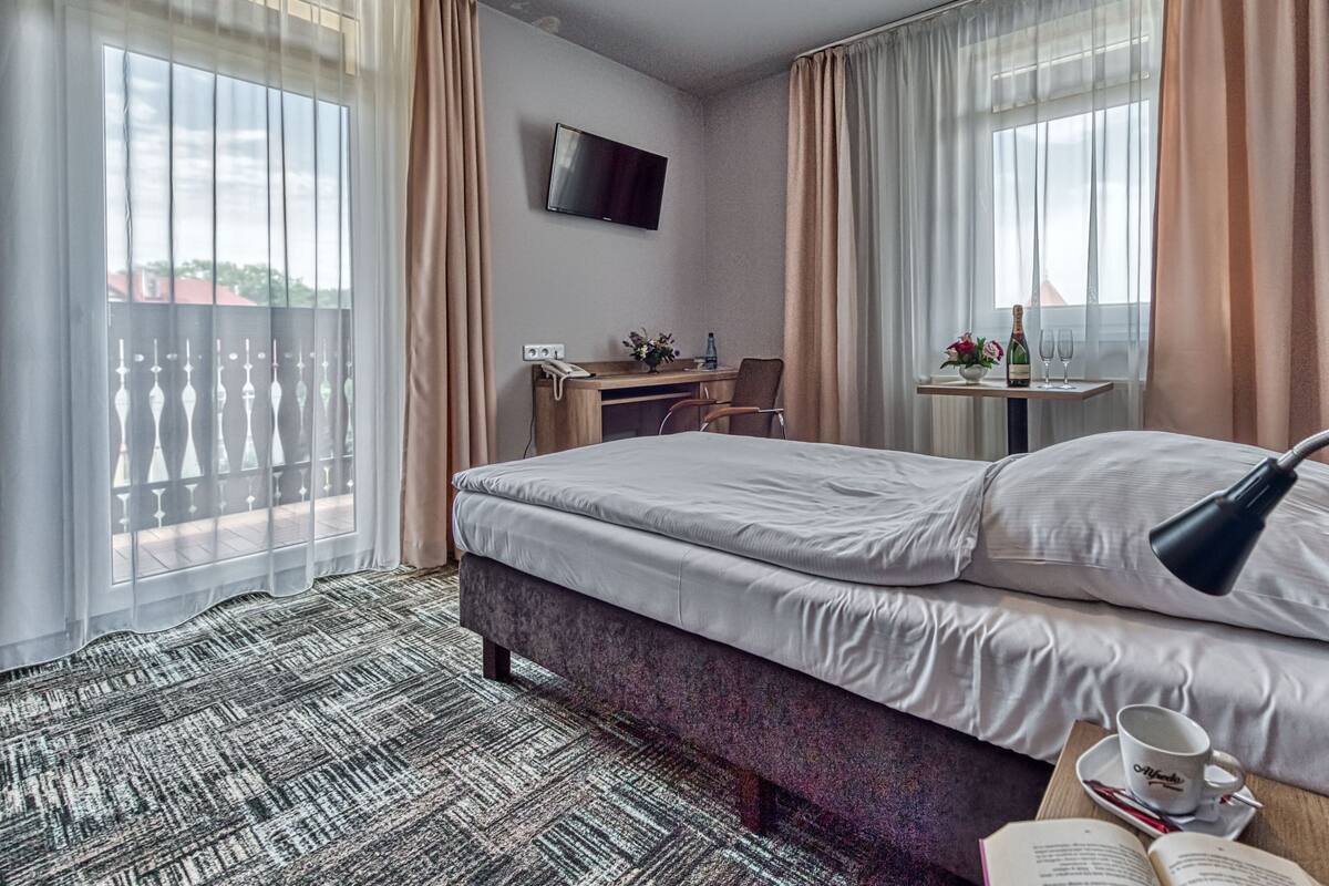 A hotel room with a bed, a desk, a TV, and a window with curtains.