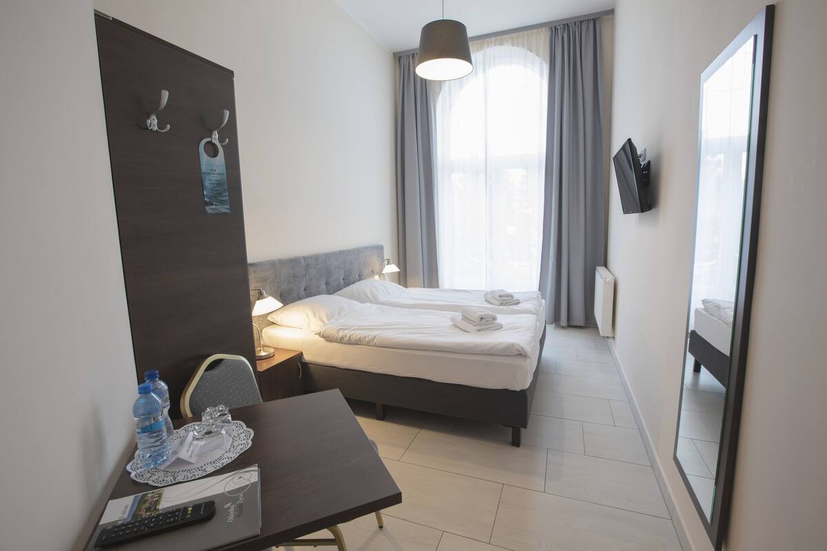 A hotel room with a bed, bedside table, lamp, and a large window with curtains.