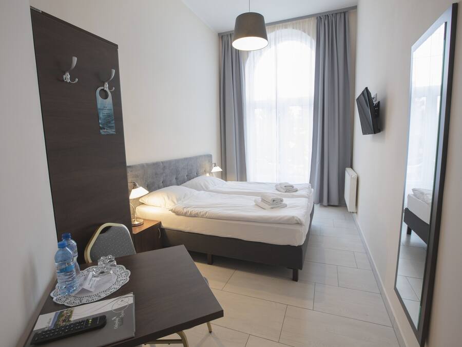 A hotel room with a bed, bedside table, lamp, and a large window with curtains.