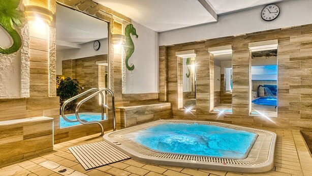 A spa area with a hot tub, a mirror wall, and a clock on the wall. - St. Lukas Medical & SPA (Swieradow-Zdroj)