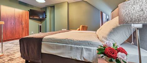 Un dormitorio con cama, televisión, lámpara y un jarrón con flores.