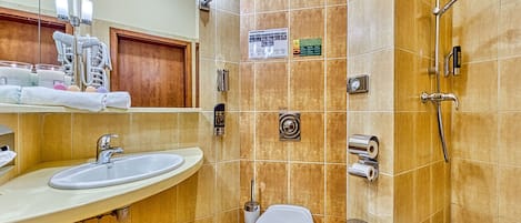 A bathroom with a sink, toilet, and shower. There are towels and a soap dispenser on the sink counter.