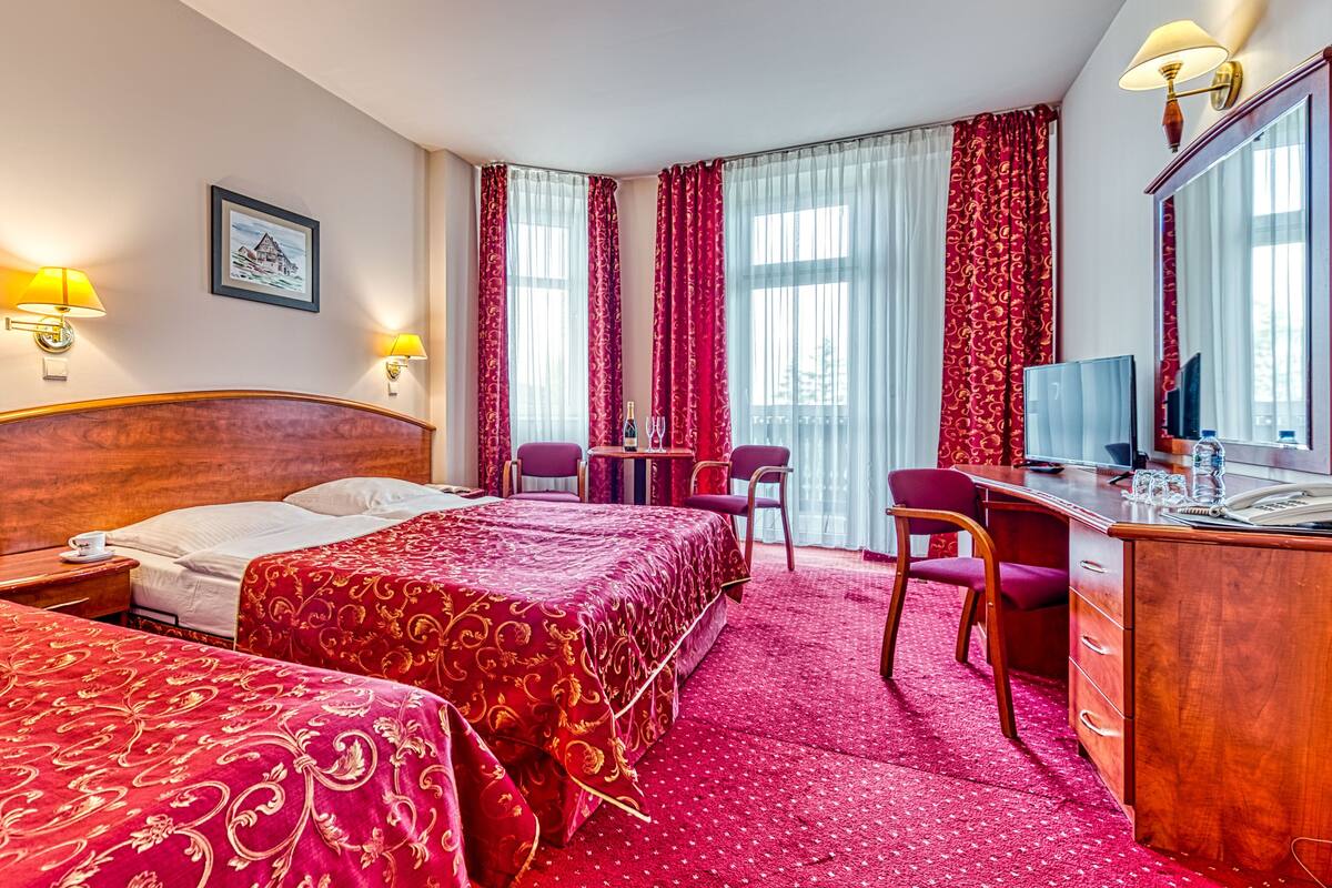 A hotel room with two beds, a desk, a chair, a television, and a window with curtains.