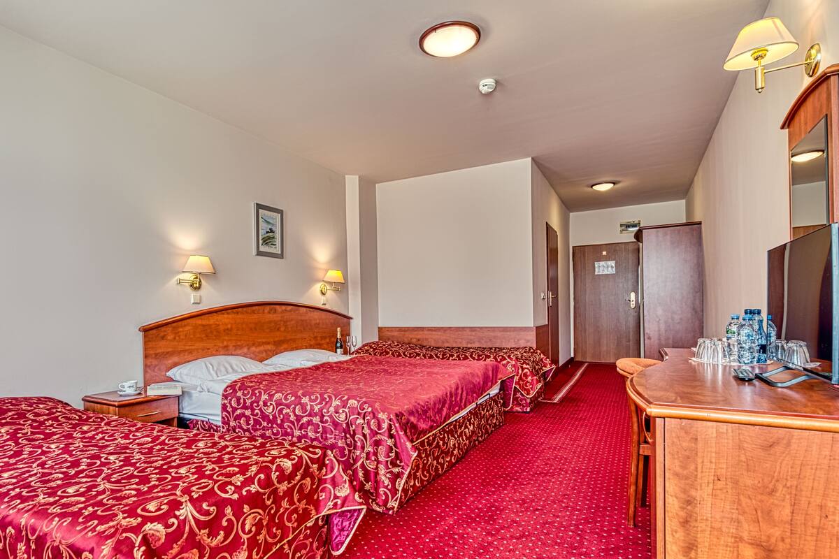 A hotel room with two beds, a wooden dresser, a mirror, and a red carpet.