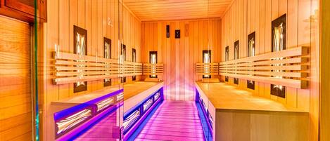A sauna with wooden walls and benches, a central walkway, and a ceiling with a light fixture.
