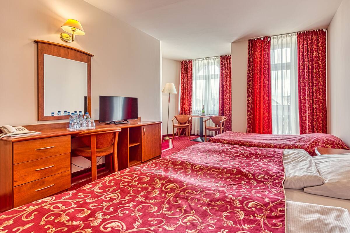 A hotel room with two beds, a desk, a chair, a television, and a telephone.