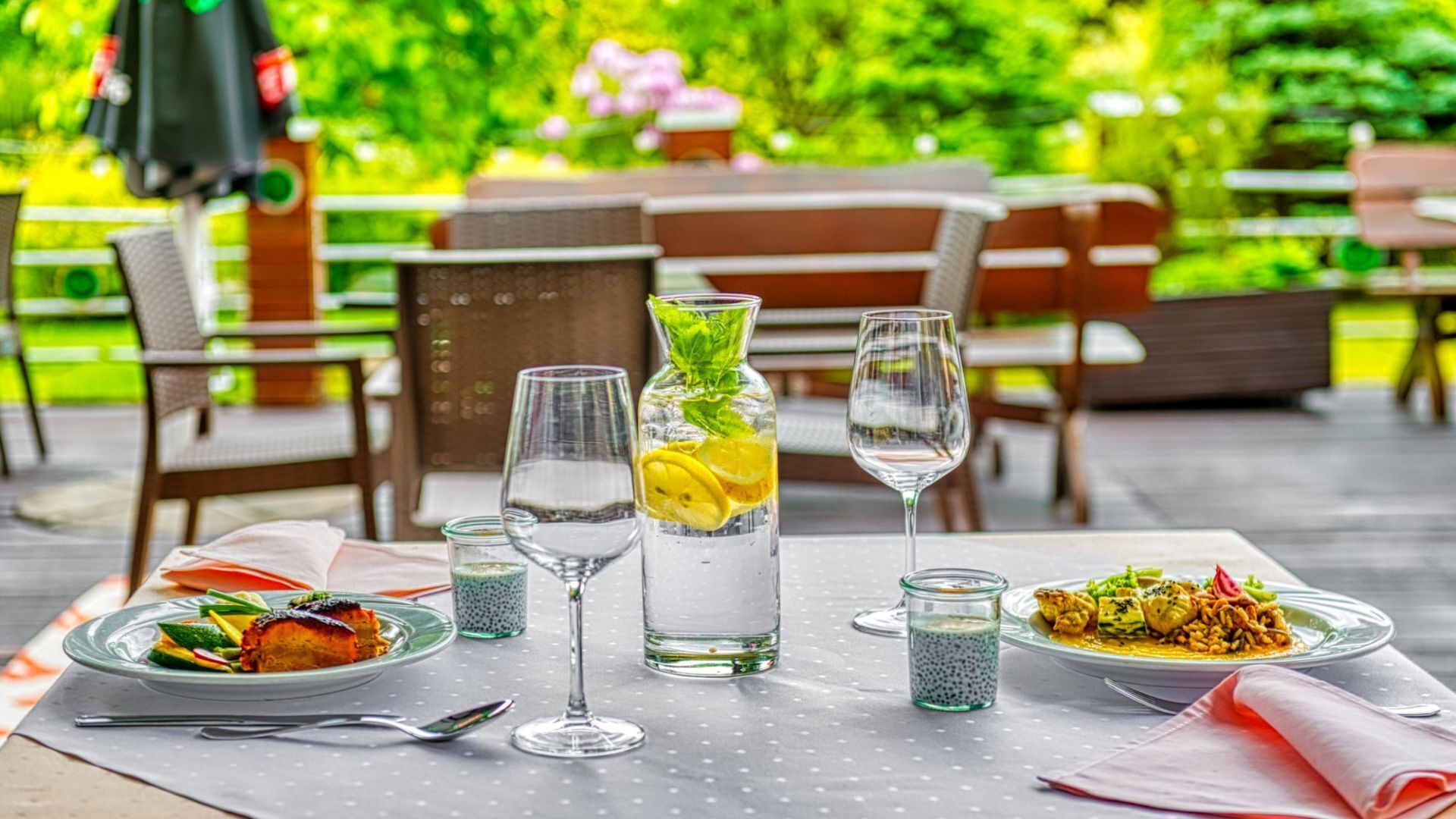 Una mesa de comedor con dos platos de comida, dos vasos de agua y una botella con una rodaja de limón.
