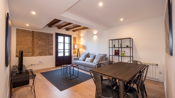 Una sala de estar moderna con un sofá, una mesa de comedor con sillas, un televisor y una estantería.