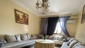 Ein Wohnzimmer mit einer Sofagarnitur, einem runden Couchtisch, einer Pendelleuchte und einem Bild an der Wand.