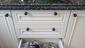 Une cuisine avec un plan de travail noir à motifs, une bouilloire, une poêle verte et un tiroir contenant des casseroles.