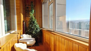 Une pièce aux murs lambrissés, avec vue sur des immeubles, un sapin de Noël et une petite table entourée de chaises.