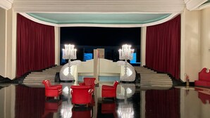 Un vaste hall d’entrée avec un sol réfléchissant, des fauteuils rouges et un escalier menant à un balcon.
