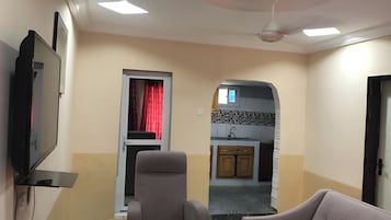 Una sala de estar con televisor, sofá y una cocina visible a través de un arco.