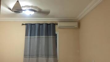 A room with a ceiling fan, an air conditioning unit, and a curtain.