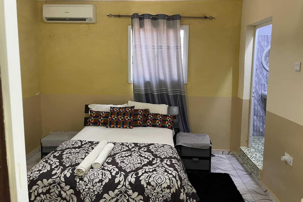 Une chambre à coucher comprenant un lit, des tables de chevet, un appareil de climatisation, une fenêtre avec des rideaux et une vue sur un balcon.