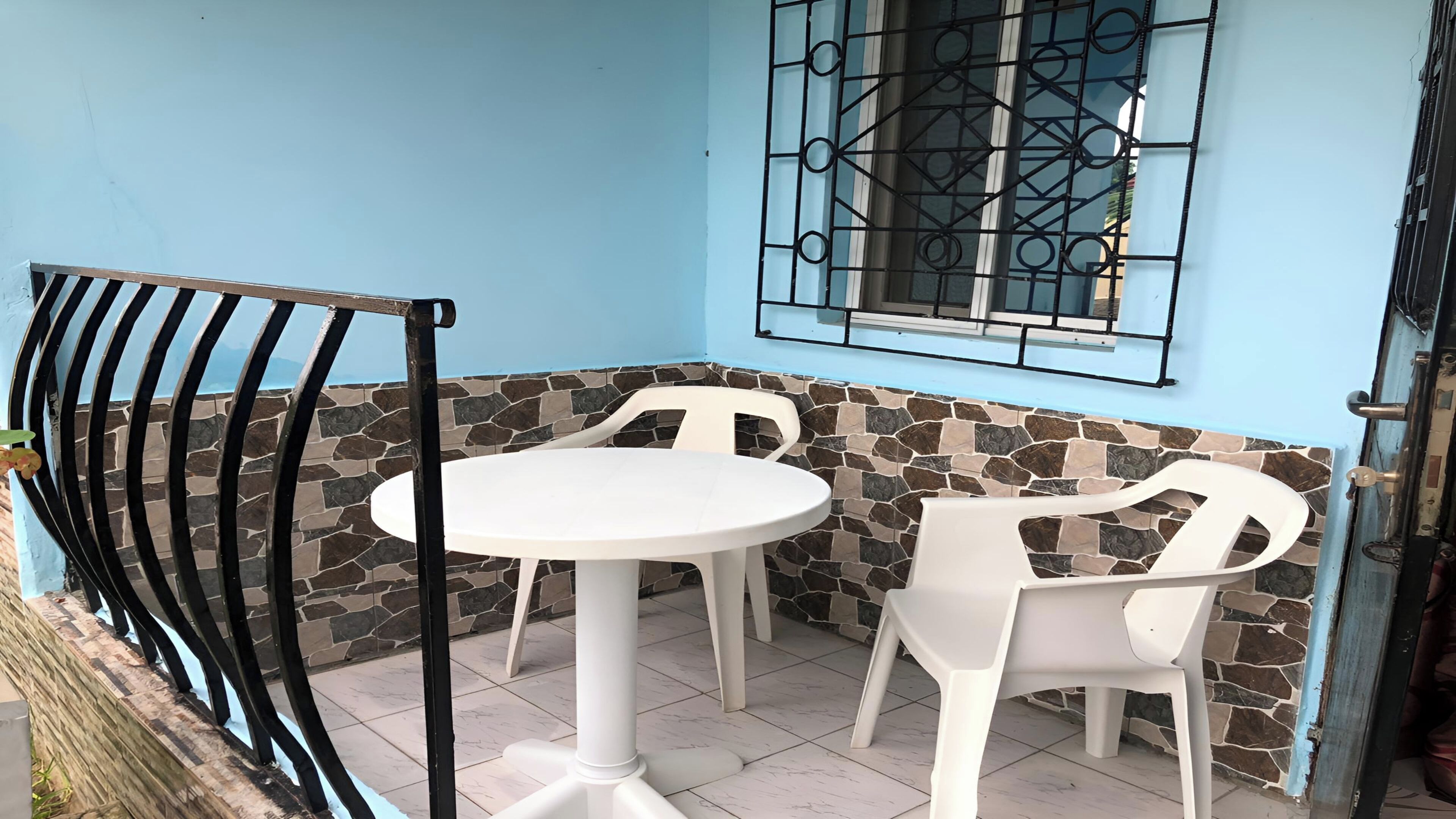 A small patio with a white table and two chairs, a stone wall, and a metal gate.