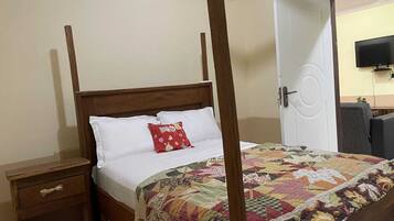 A bedroom with a four-poster bed, a wooden nightstand, a red pillow, and a quilted bedspread.