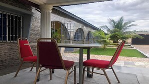 A patio with a table and two red chairs, a stone wall, and a view of a building with arched windows.