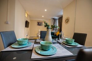 A dining table set with green bowls and plates, a vase with greenery, and a flat-screen TV mounted on the wall.