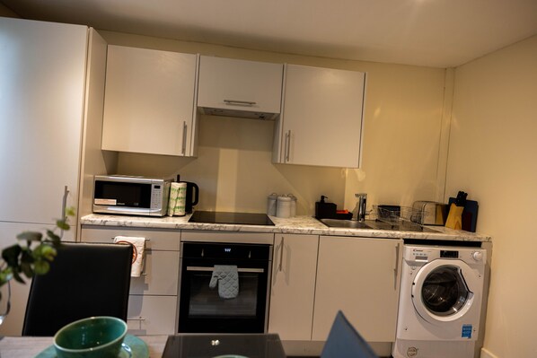 A compact kitchen with white cabinets, a microwave, a dishwasher, and a washing machine. - 3 Bedrooms-8guests-babycot-15mintopepys-freeparkg (London)