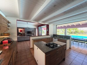 A modern kitchen with a central island, wooden cabinets, and a view of a swimming pool.