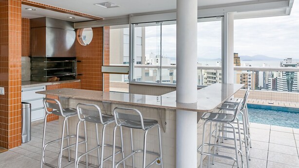 A modern kitchen with a built-in oven and a bar area with stools. - WI-FI 180MB | 200m from Beiramar Shopping #CA52 (Florianópolis)