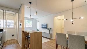 A modern kitchen with a wooden island, bar stools, and a dining area with grey upholstered chairs. - WI-FI 180MB | 200m from Beiramar Shopping #CA52 (Florianópolis)
