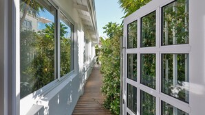A narrow corridor with wooden flooring, white walls, and large windows on both sides.