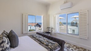 A bedroom with a bed, two windows, a chair, and a view of the sea.