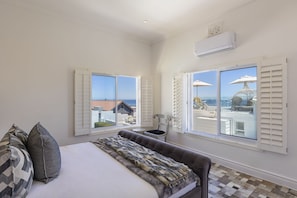 A bedroom with a bed, two windows, an air conditioning unit, and a view of the sea. - Clifton YOLO Spaces : Clifton Boutique Apartment A (Cape Town)
