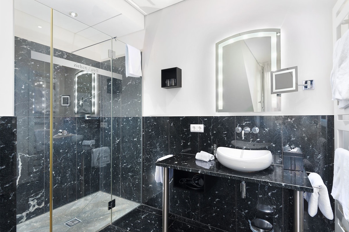 Un baño moderno con ducha de vidrio, un lavabo blanco y un espejo grande.