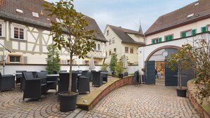 A courtyard with outdoor seating, cobblestone flooring, and traditional European architecture.