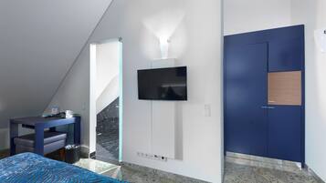 Una habitación de hotel moderna con una cama, un escritorio, un televisor montado en la pared y un armario.