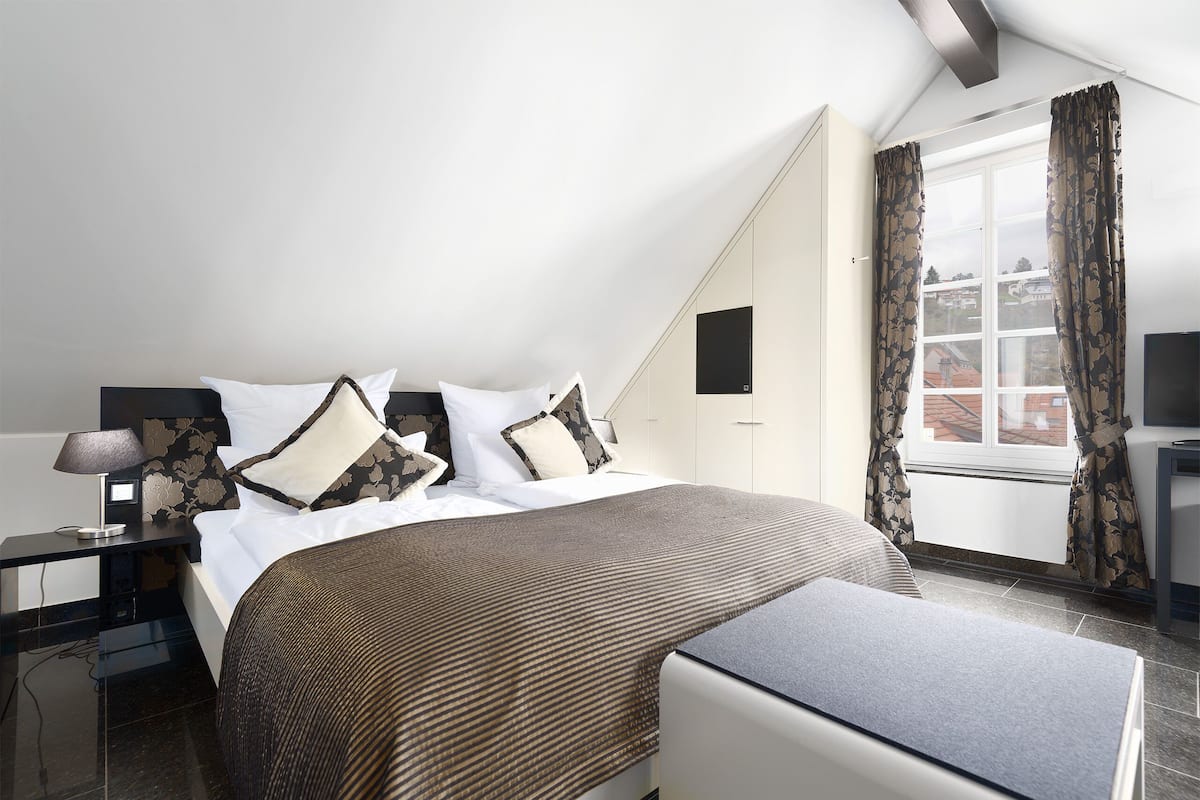 Un dormitorio con cama, mesita de noche, lámpara y vistas al exterior por una ventana.