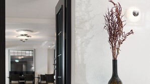 A modern hallway with a tiled floor, a vase with dried plants on a console table, and a door leading to a dining area.