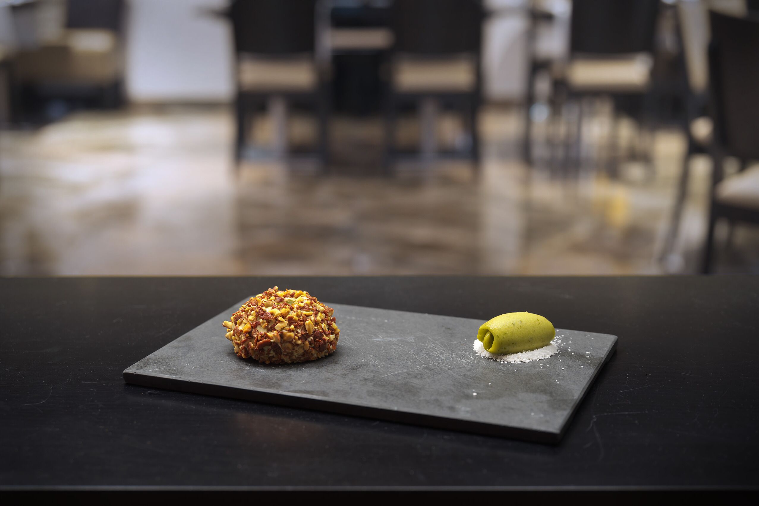 Un dessert su un piatto di ardesia in una sala da pranzo con pavimento lucido e sedie sullo sfondo.