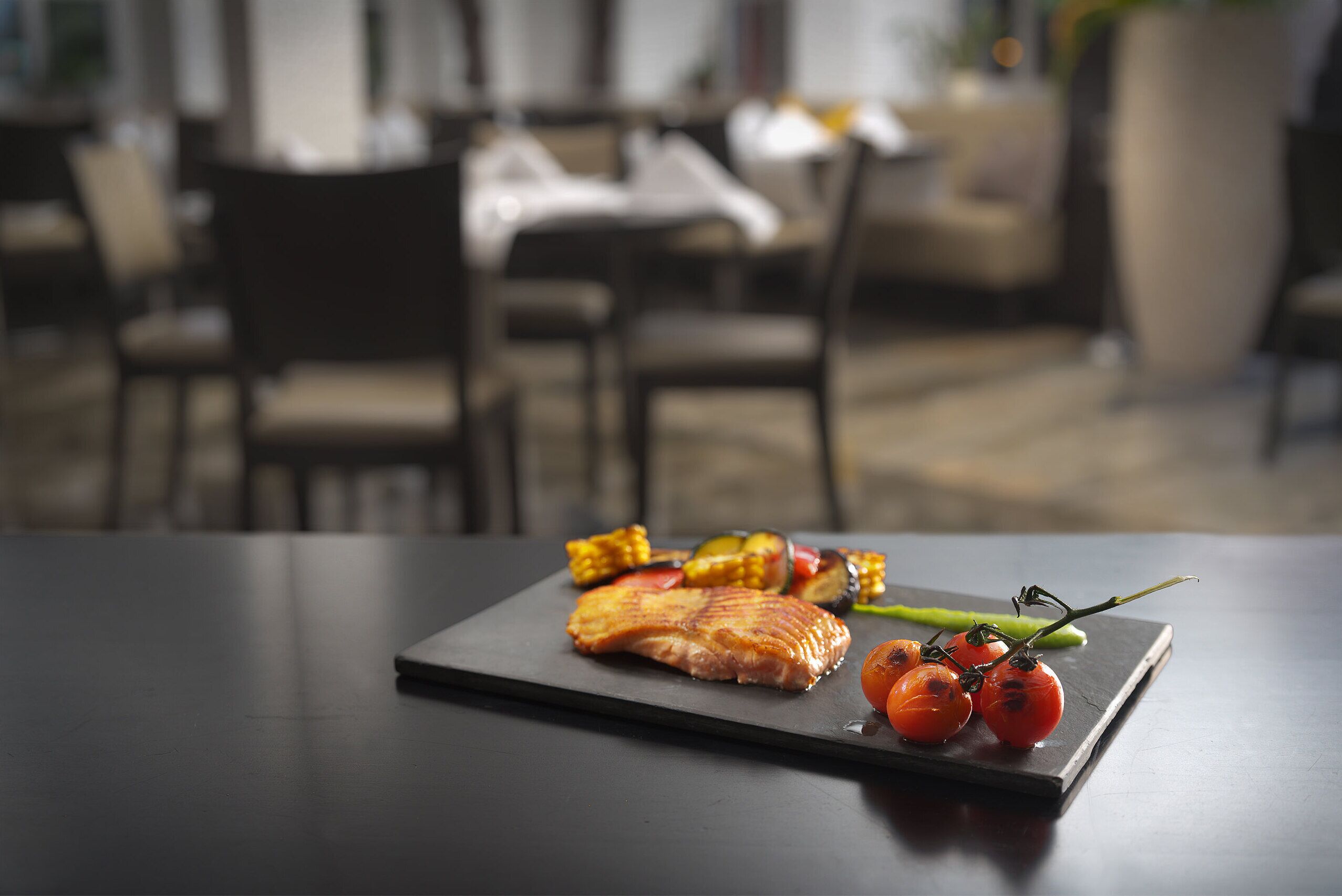 A dining table with a salmon fillet, corn, cherry tomatoes, and asparagus.